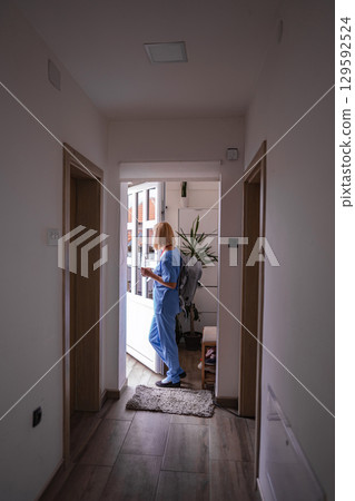 Female doctor wearing blue scrubs standing at the entrance of a house Female doctor wearing blue scrubs standing at the entrance of a house 129592524