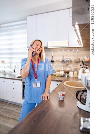 Smiling female doctor talking on the phone during coffee break in the kitchen 129592525