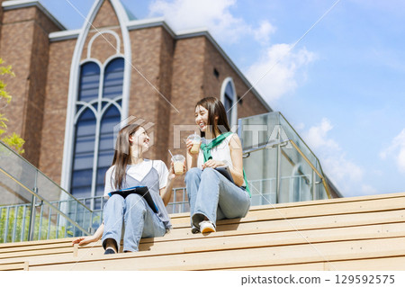 大學生和朋友坐在校園樓梯的長椅上 大學生和朋友坐在校園樓梯的長椅上 129592575