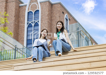 大學生和朋友坐在校園樓梯的長椅上 大學生和朋友坐在校園樓梯的長椅上 129592577