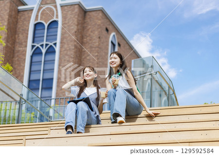 College student sitting on a bench on campus stairs with friends College student sitting on a bench on campus stairs with friends 129592584