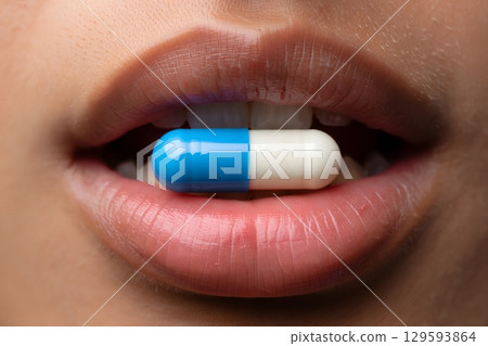 Close-up of blue and white capsule held between teeth, medicine or supplement concept with shallow focus 129593864