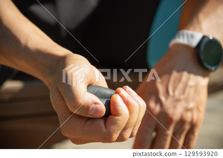 Man strengthens his grip using hand black rubber expander. He is seen holding expander with firm grip, suggesting focused exercise. Close up. 129593920