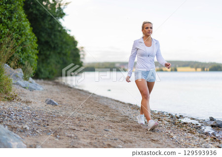 Woman walking on a scenic lakeside trail in a sporty fitness outfit Woman walking on a scenic lakeside trail in a sporty fitness outfit 129593936