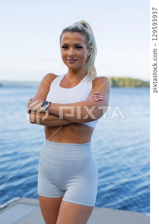 Confident woman in athletic wear by the water during outdoor workout 129593937