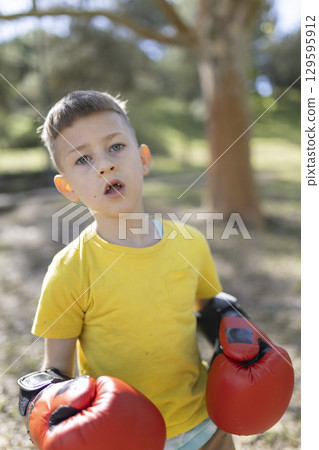 Young boy wearing boxing gloves posing in a park Young boy wearing boxing gloves posing in a park 129595912