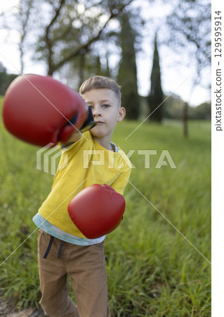 Young boy wearing boxing gloves throws a punch in the park Young boy wearing boxing gloves throws a punch in the park 129595914