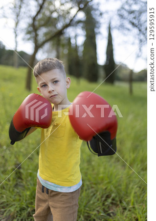 Young boy wearing boxing gloves practicing in park Young boy wearing boxing gloves practicing in park 129595915