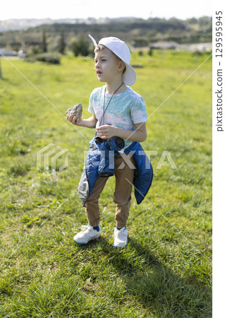 Curious youngster exploring nature holding a rock in a field Curious youngster exploring nature holding a rock in a field 129595945