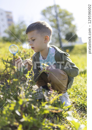 Curious child exploring nature with magnifying glass in a sunny park 129596002