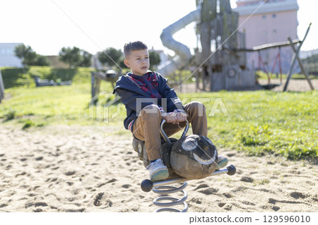 Child playing on spring rider at playground on sunny day Child playing on spring rider at playground on sunny day 129596010