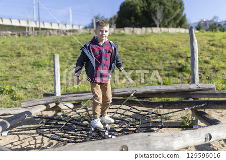 Young boy balancing on rope net at playground in sunny day 129596016