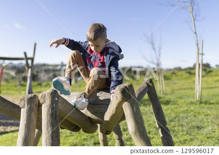 Child playing on wooden spider in playground, enjoying outdoor fun 129596017