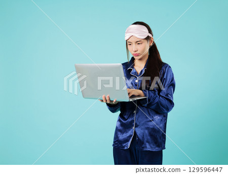 Angry woman in pajama mask, overworked from remote work on laptop computer, wants to sleep, young as she may be, and to avoid more work and go back to sleep, headshots isolated studio blue background Angry woman in pajama mask, overworked from remote work on laptop computer, wants to sleep, young as she may be, and to avoid more work and go back to sleep, headshots isolated studio blue background 129596447