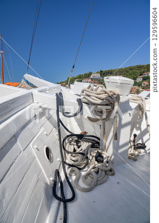 Close-up of ropes on a white wooden boat deck under blue sky Close-up of ropes on a white wooden boat deck under blue sky 129596604