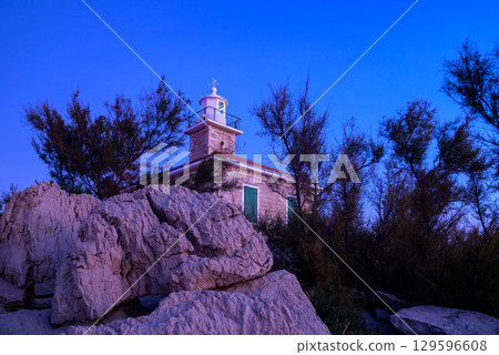 Lighthouse at dusk surrounded by coastal rocks and vegetation Lighthouse at dusk surrounded by coastal rocks and vegetation 129596608
