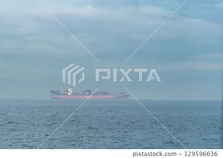 A large cargo ship sailing on a calm sea under a cloudy sky in Osaka bay, Osaka, Japan A large cargo ship sailing on a calm sea under a cloudy sky in Osaka bay, Osaka, Japan 129596636