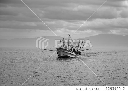 A lone fishing boat on a calm sea under a cloudy sky in Osaka bay in Japan A lone fishing boat on a calm sea under a cloudy sky in Osaka bay in Japan 129596642