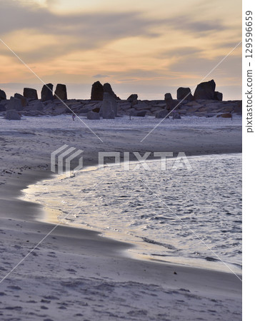 Scenic coastal view with calm sea, sandy beach, and rock formations under a vibrant sky at sunset Scenic coastal view with calm sea, sandy beach, and rock formations under a vibrant sky at sunset 129596659