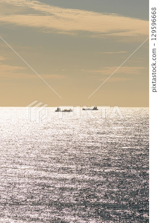 Cargo ships on a shimmering sea under a sunset sky 129596668