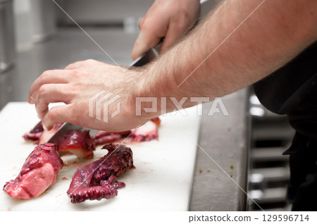 Slicing fresh octopus tentacle with a sharp knife on a white cutting board, delicate seafood Slicing fresh octopus tentacle with a sharp knife on a white cutting board, delicate seafood 129596714