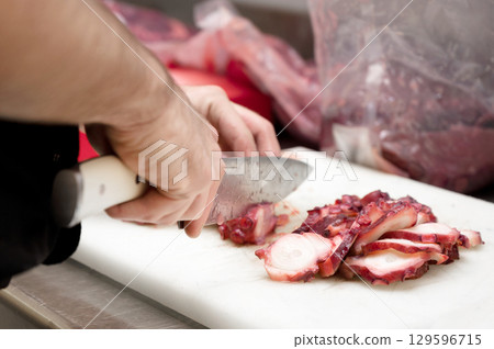 Slicing fresh octopus tentacle with a sharp knife on a white cutting board, delicate seafood 129596715