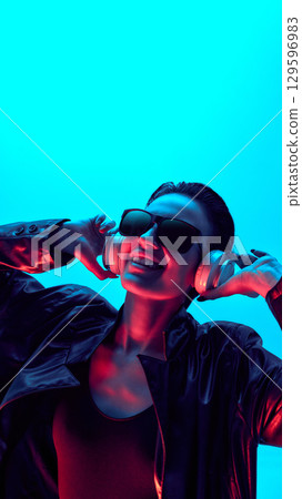 Stylish woman in neon light with headphones and joyful smile 129596983
