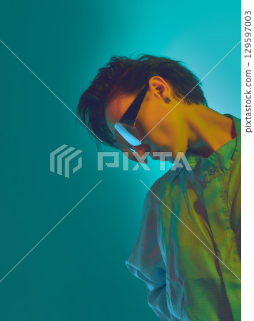 Stylish woman in neon red visor with downward head tilt against blue light Stylish woman in neon red visor with downward head tilt against blue light 129597003