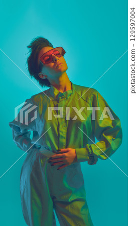 Woman in oversized shirt posing in neon red sunglasses on cyan background 129597004