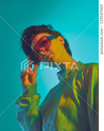 Woman adjusting red visor sunglasses under teal and yellow light 129597005