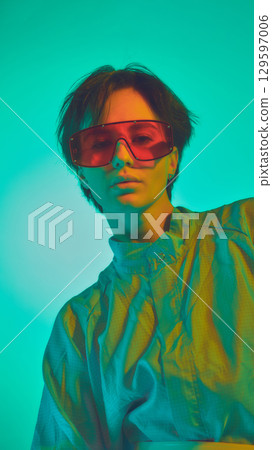 Woman in oversized shirt and red visor glasses under vivid teal light Woman in oversized shirt and red visor glasses under vivid teal light 129597006