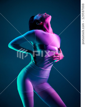 Woman in white bodysuit arching back under neon cyan and magenta light 129597008