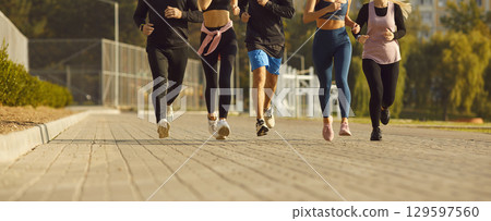 Cropped photo of a people jogging along a path in the park having sport workout in nature. Cropped photo of a people jogging along a path in the park having sport workout in nature. 129597560