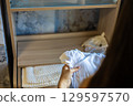 Pregnant woman is carefully holding a white baby bodysuit, organizing clothes and accessories in a modern nursery, preparing for the imminent arrival of her newborn. 129597570