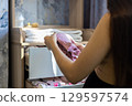 A pregnant woman folds and arranges pink baby clothes in a dresser drawer in preparation for the arrival of her newborn creating a cozy and organized nursery Woman preparing for the birth of a child. 129597574