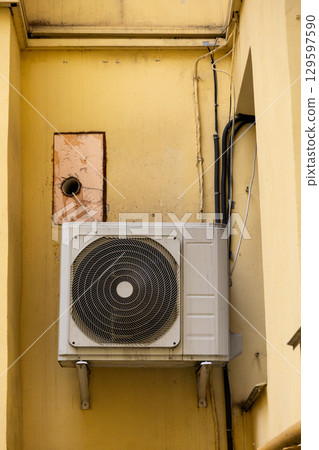 dirty air conditioner unit is mounted on a yellow wall. ventilation and cooling of the home. dirty air conditioner unit is mounted on a yellow wall. ventilation and cooling of the home. 129597590