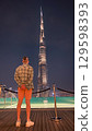 Man admires Burj Khalifa at night from a rooftop pool deck.  129598393