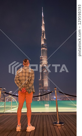Man admires Burj Khalifa at night from a rooftop pool deck. Man admires Burj Khalifa at night from a rooftop pool deck. 129598393