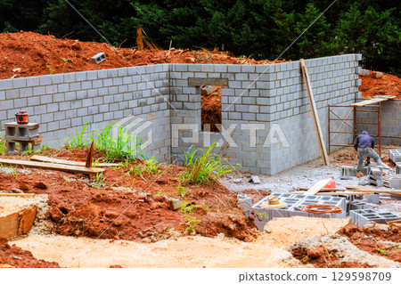 Construction progress on residential building foundation in wooded area during work day hours 129598709