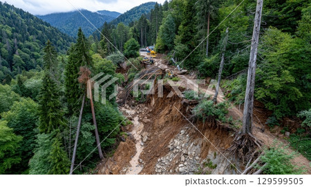 Landslide debris removal operation in progress on a mountain road, with heavy machinery clearing the path amidst damaged trees and exposed soil 129599505
