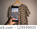 Close up of hands holding smartphone camera capturing old clothes items for online resale resources. Image for second hand concept. 129599935