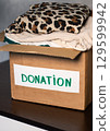 Woman folding clothes and placing them into donation box. Concept of charity and wardrobe decluttering. 129599942