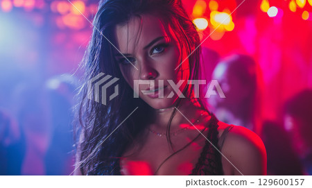 Attractive female dancing near vibrant lighting, surrounded by nightclub crowd 129600157