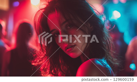 Young woman dancing under vibrant neon lighting at nightclub, wearing stylish outfit 129600159