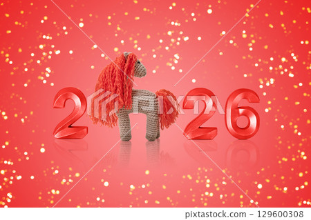 Crocheted toy fiery red horse and gold numbers. The symbol of the year 2026 on a red background. 129600308