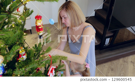 Mother and daughter happily trim a festive christmas tree, making special memories in their warm home. New Year's Eve with family 129600545