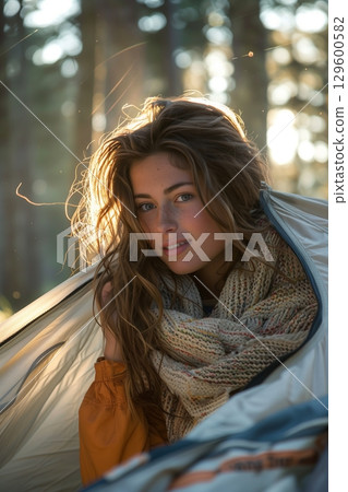 A young woman relaxes in a tent, enjoying nature and the serene atmosphere of the forest during golden hour. 129600582