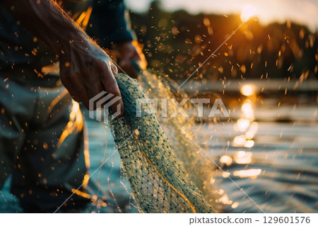A fisherman skillfully casts a net at sunset, capturing the beauty of nature and dedication to the craft. A fisherman skillfully casts a net at sunset, capturing the beauty of nature and dedication to the craft. 129601576