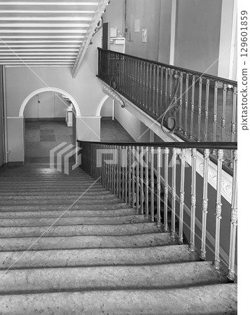 Descend a beautifully designed staircase featuring intricate railings and soft, natural light illuminating the space within a historic structure. 129601859
