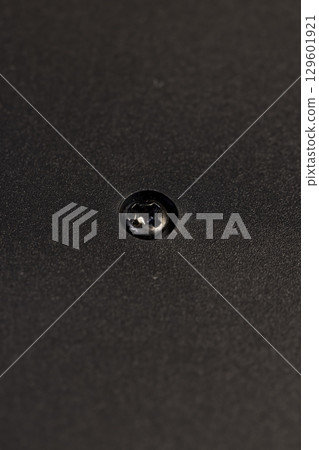 A bolt is screwed into the black plastic to connect the different parts of the object. black plastic surface, details of a part of an object made of black plastic 129601921